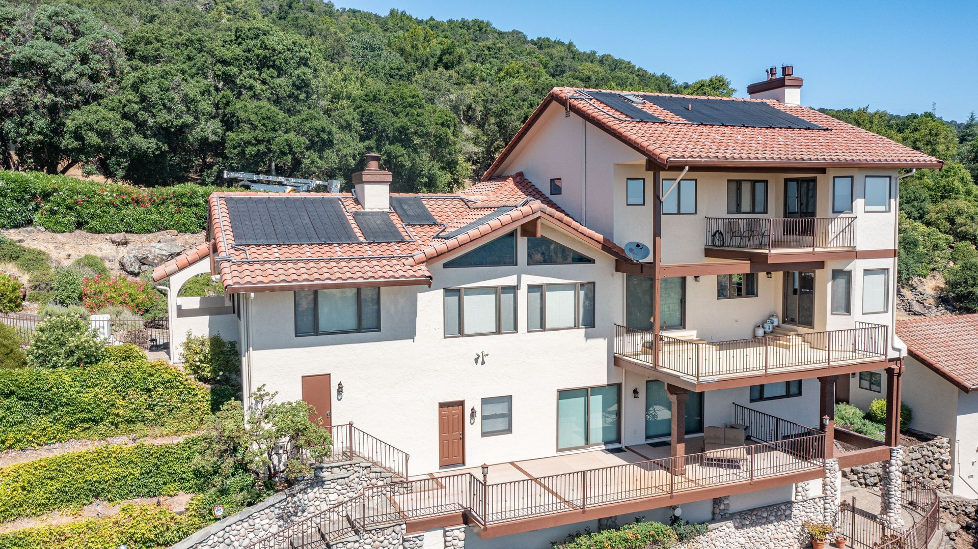 A large house with solar panels on the roof is surrounded by trees.