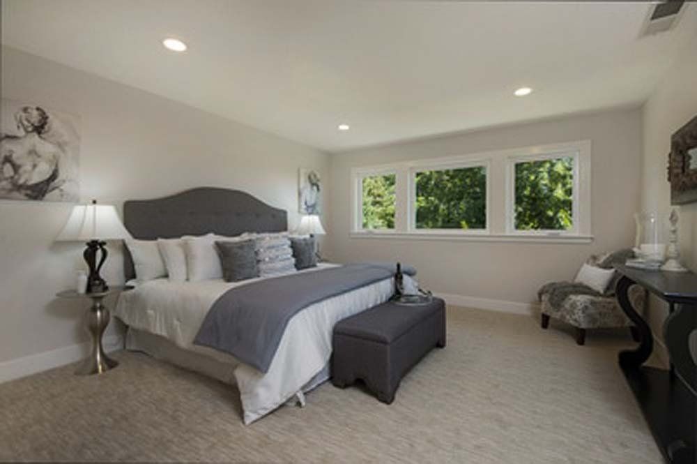 A bedroom with a king size bed , two lamps , a bench , and two windows.