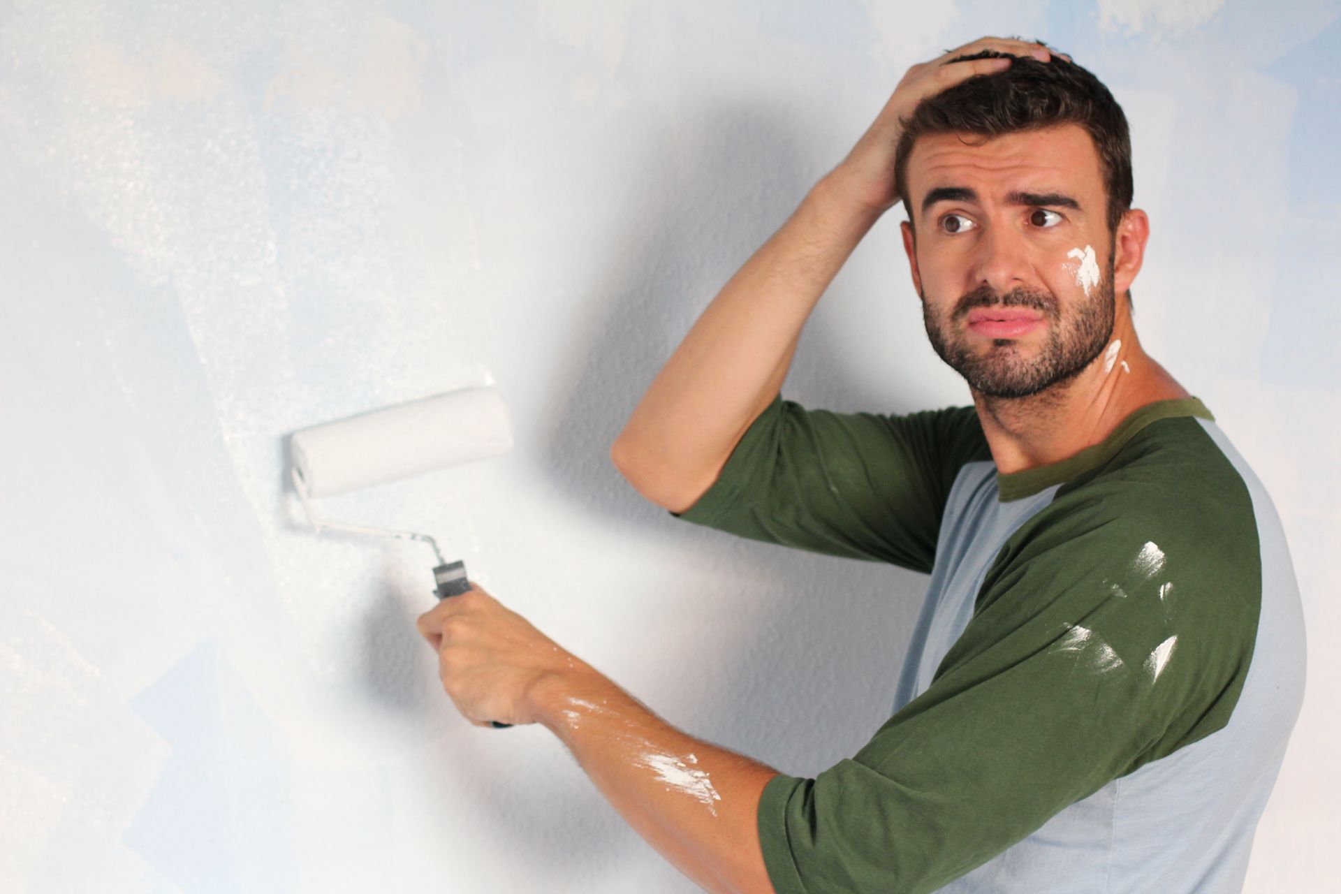 a man is painting a wall with a roller and making a funny face