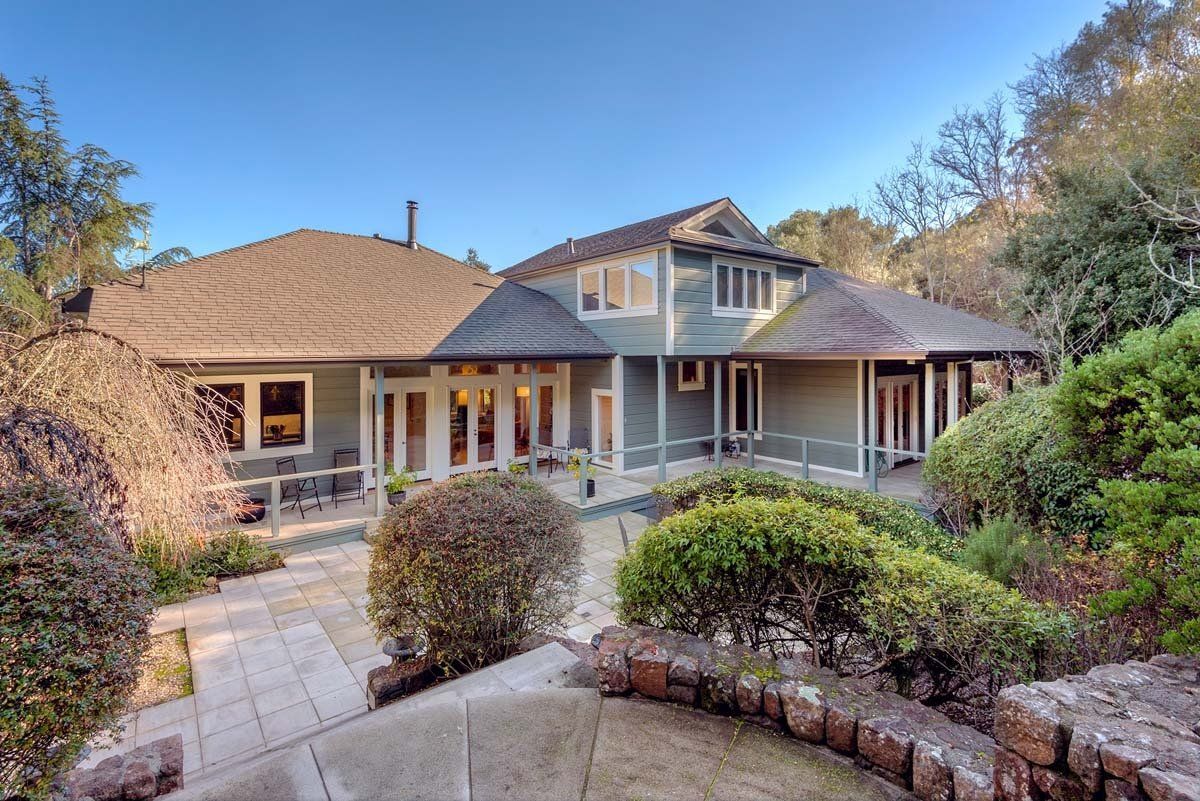 A large house with a large porch is surrounded by trees and bushes