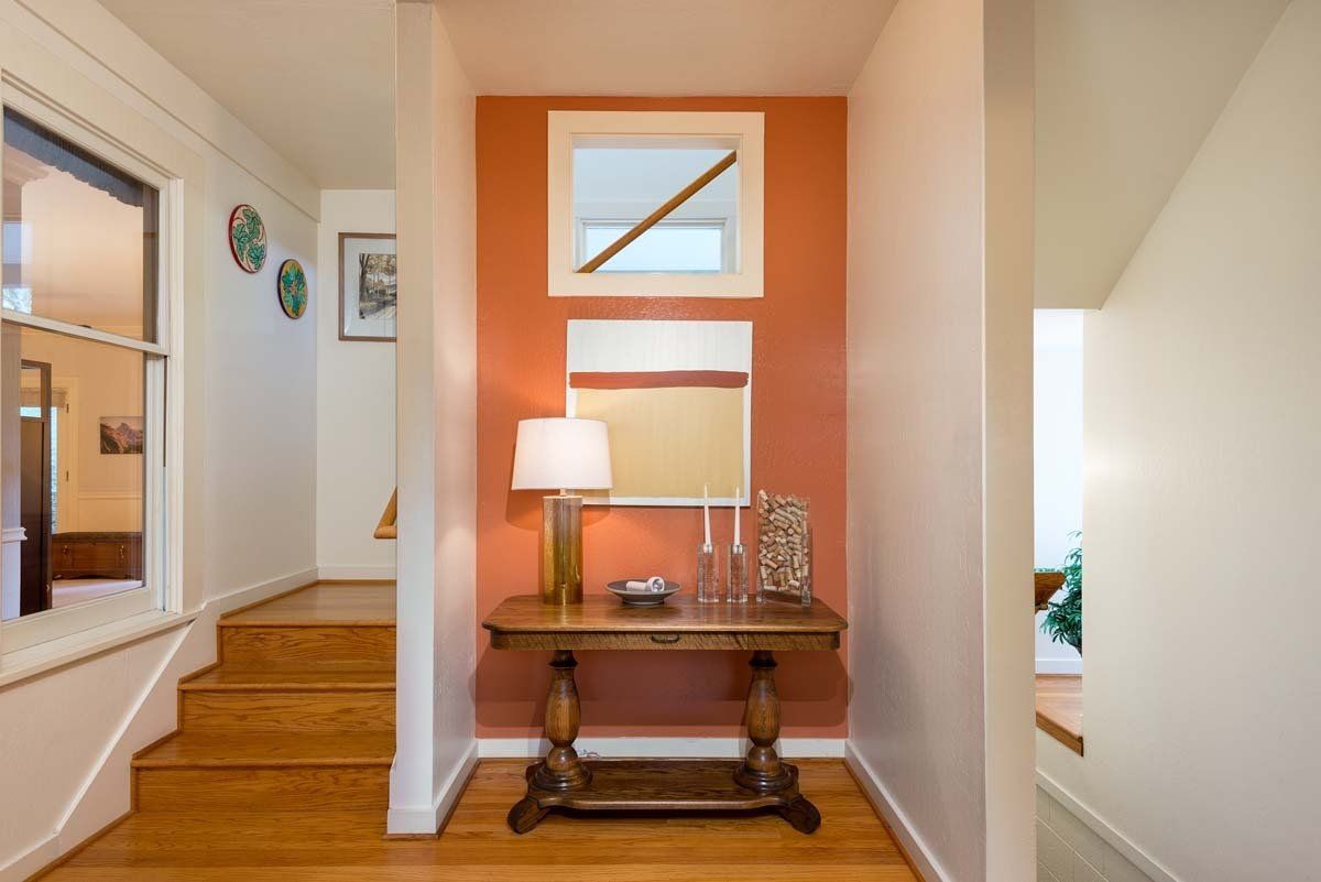 A hallway with a table , lamp , mirror and stairs.
