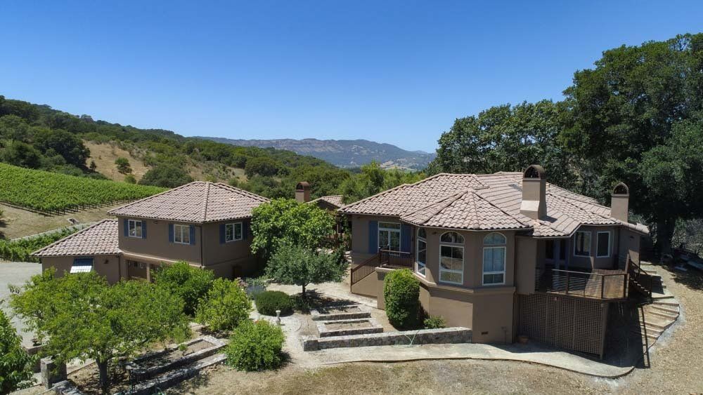 A large house sits on top of a hill in the middle of a vineyard.