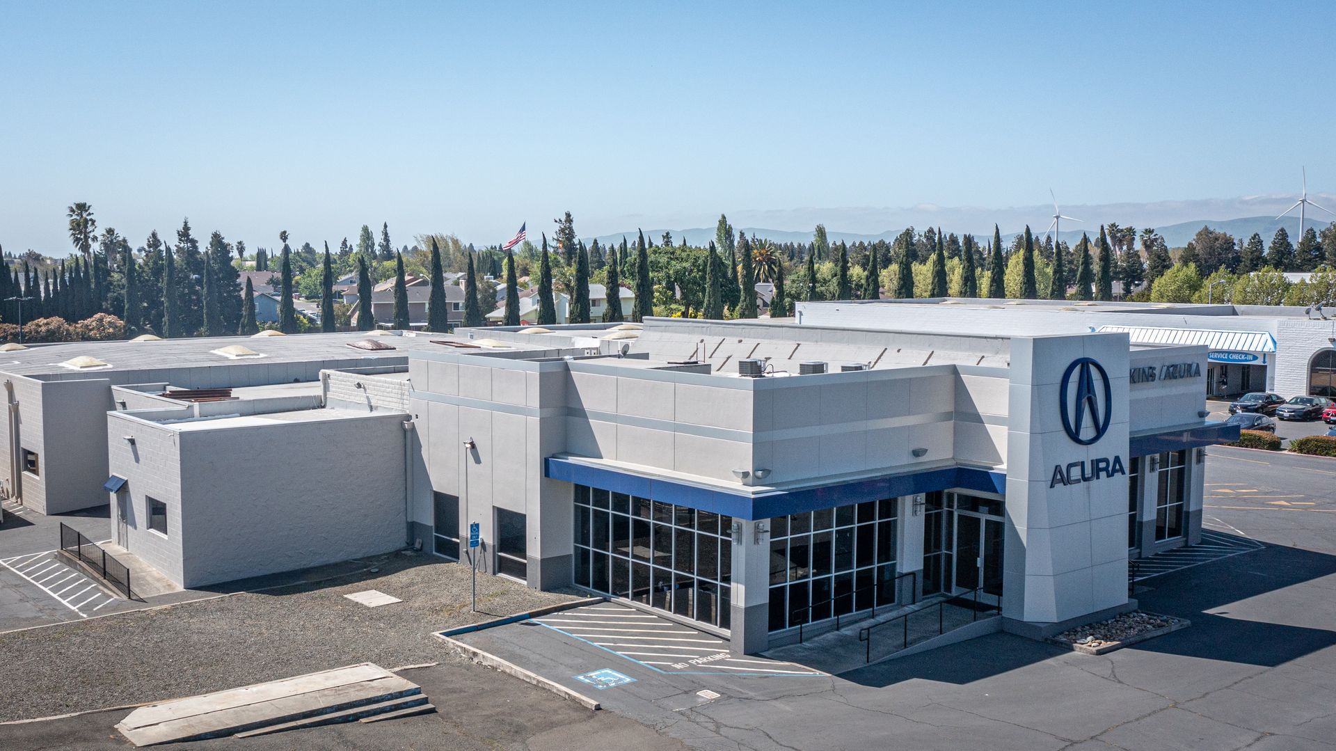 An acura dealership is sitting in a parking lot with trees in the background.