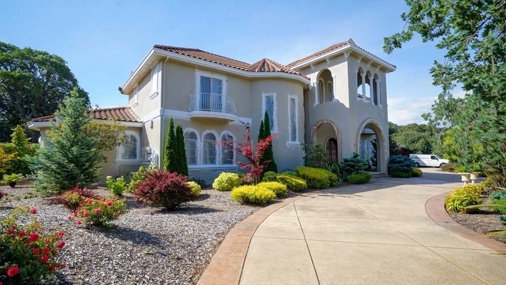 A large house with a driveway leading to it is surrounded by trees and bushes.