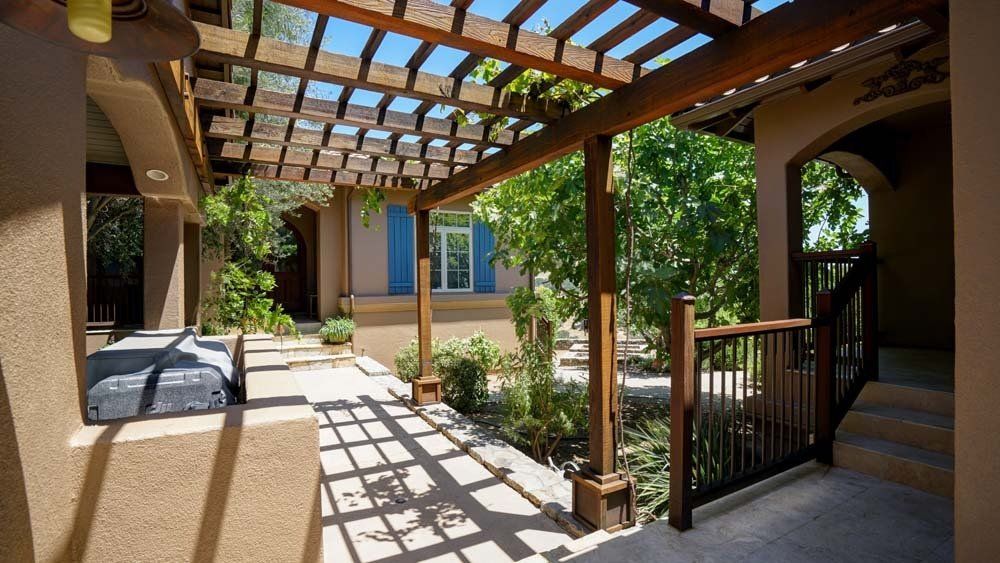 A wooden pergola over a patio in front of a house.