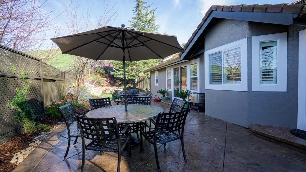 A patio with a table and chairs and an umbrella in front of a house.