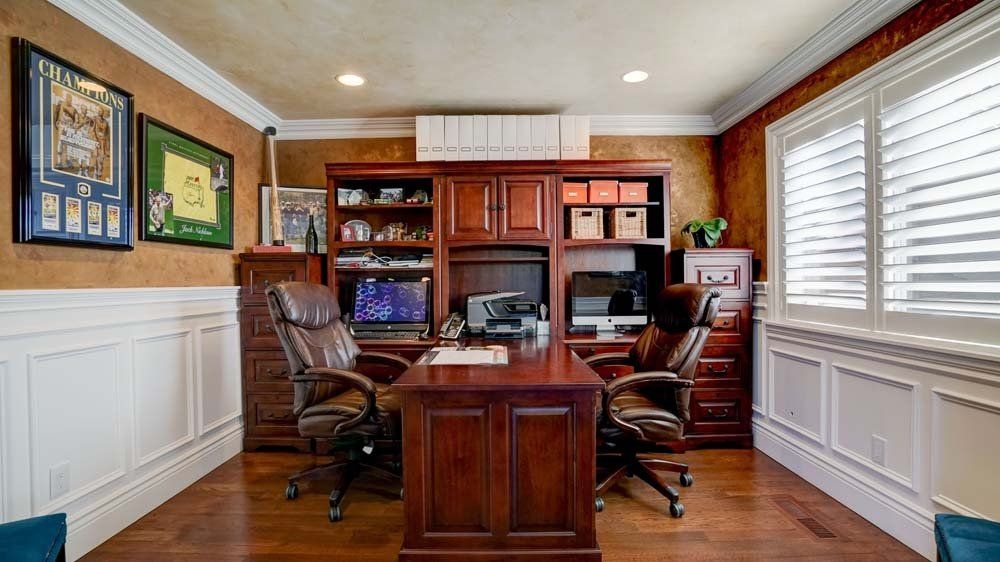 A home office with a wooden desk and two chairs.