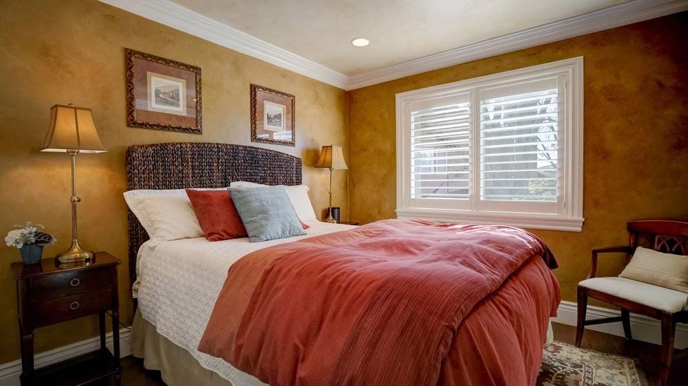 A bedroom with a bed , nightstand , lamp and window.