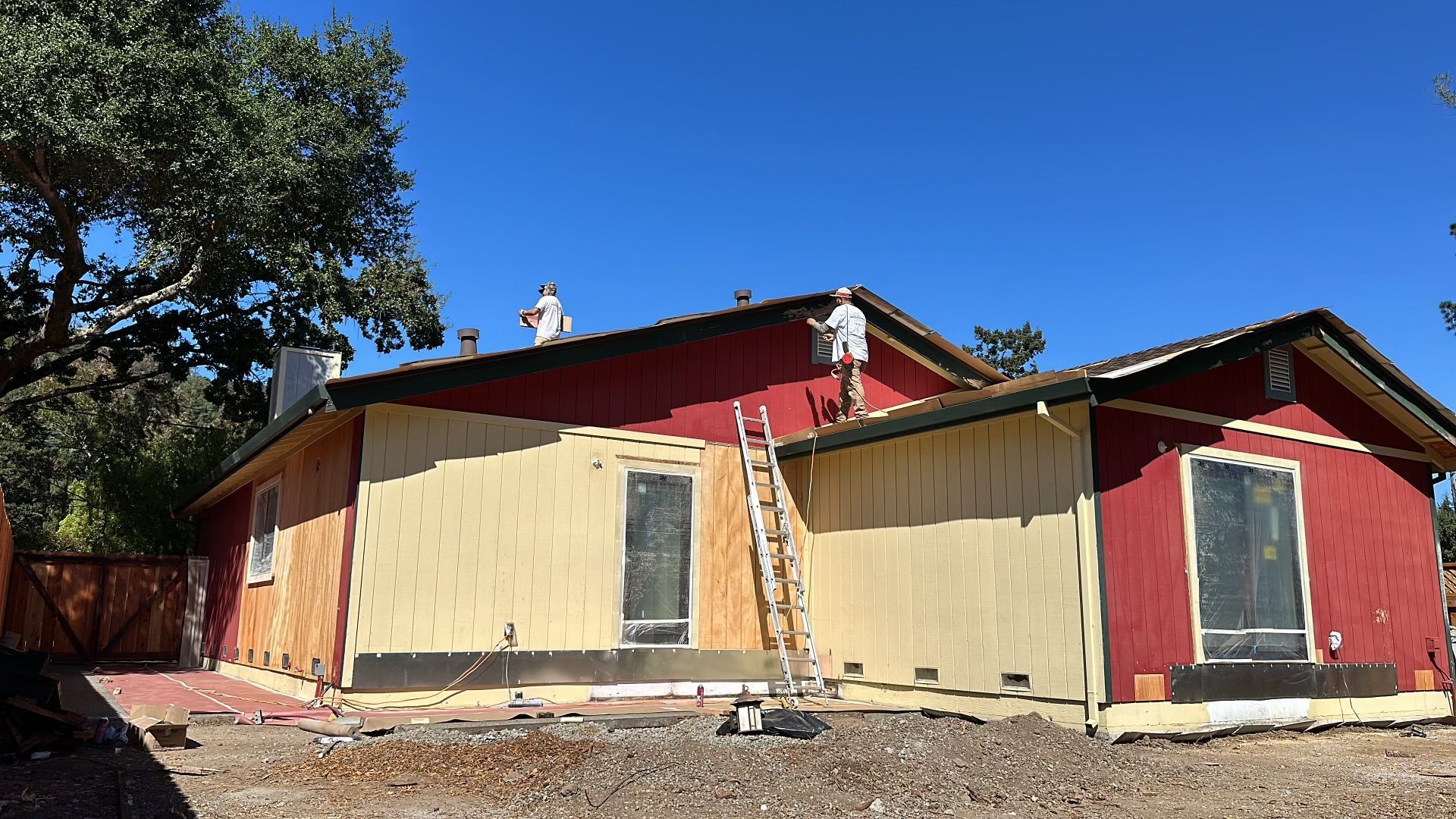 A man is painting the side of a red house.