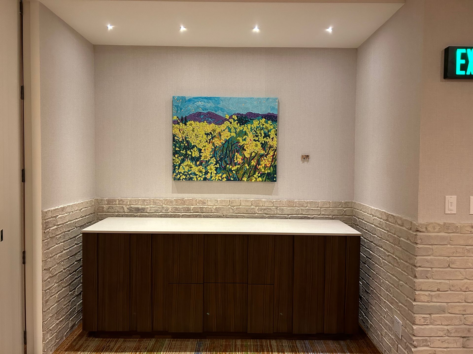 A painting of a field of yellow flowers is hanging on a wall above a counter.