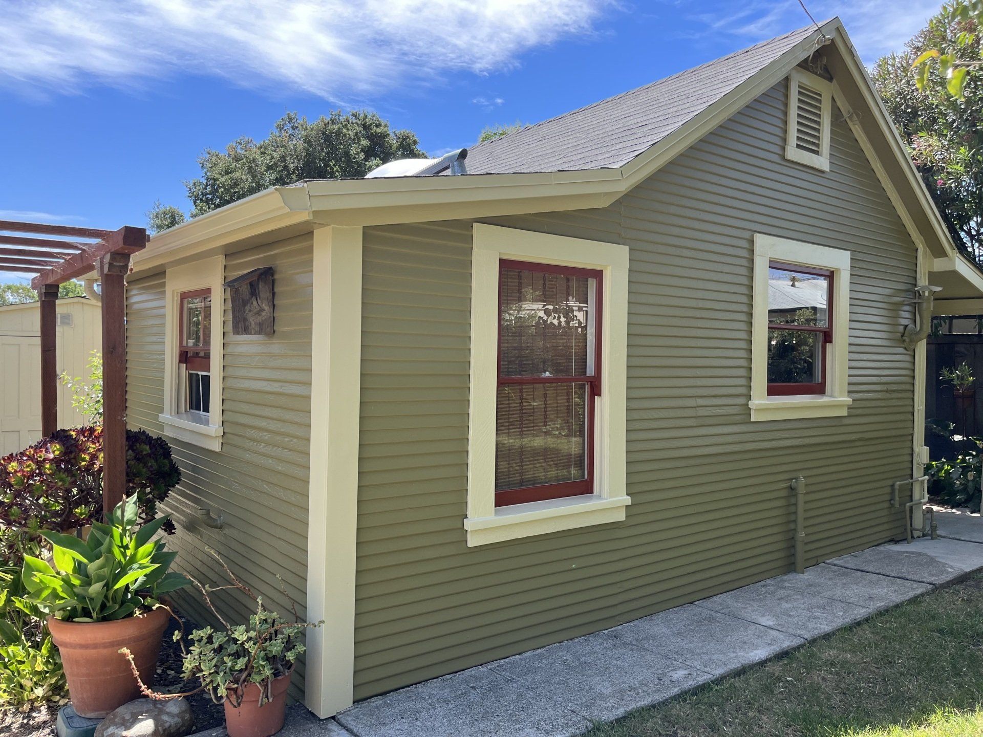 A small house with a pergola and potted plants in front of it.