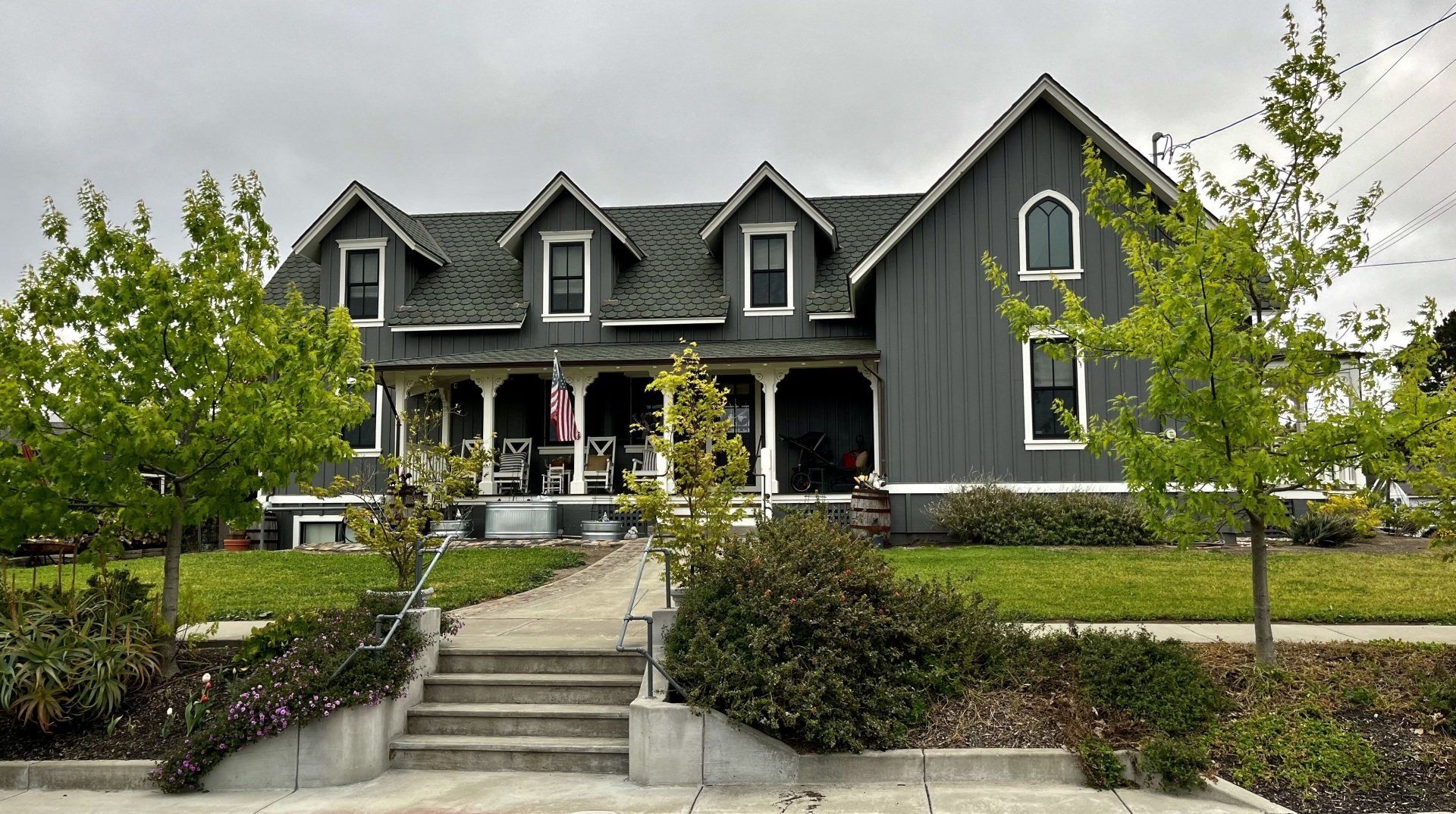 A large gray house with a green roof is surrounded by trees and bushes.