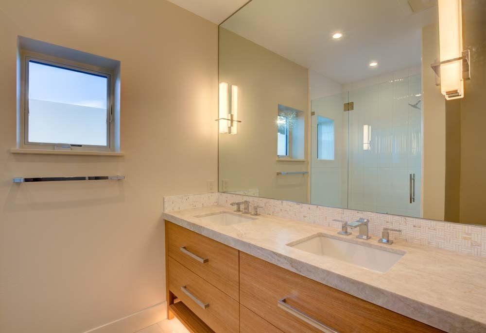 A bathroom with two sinks , a large mirror and a window.