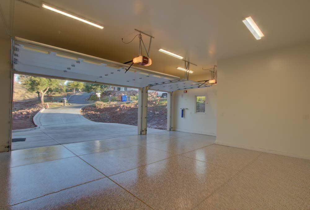 An empty garage with a garage door open and a driveway in the background.