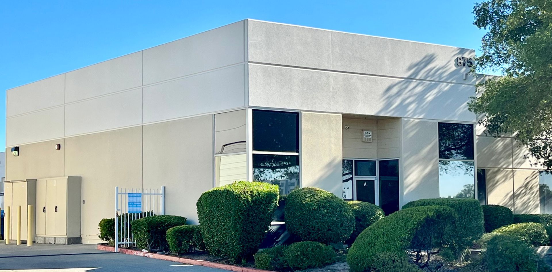 A large white building with a lot of windows is surrounded by bushes and trees.