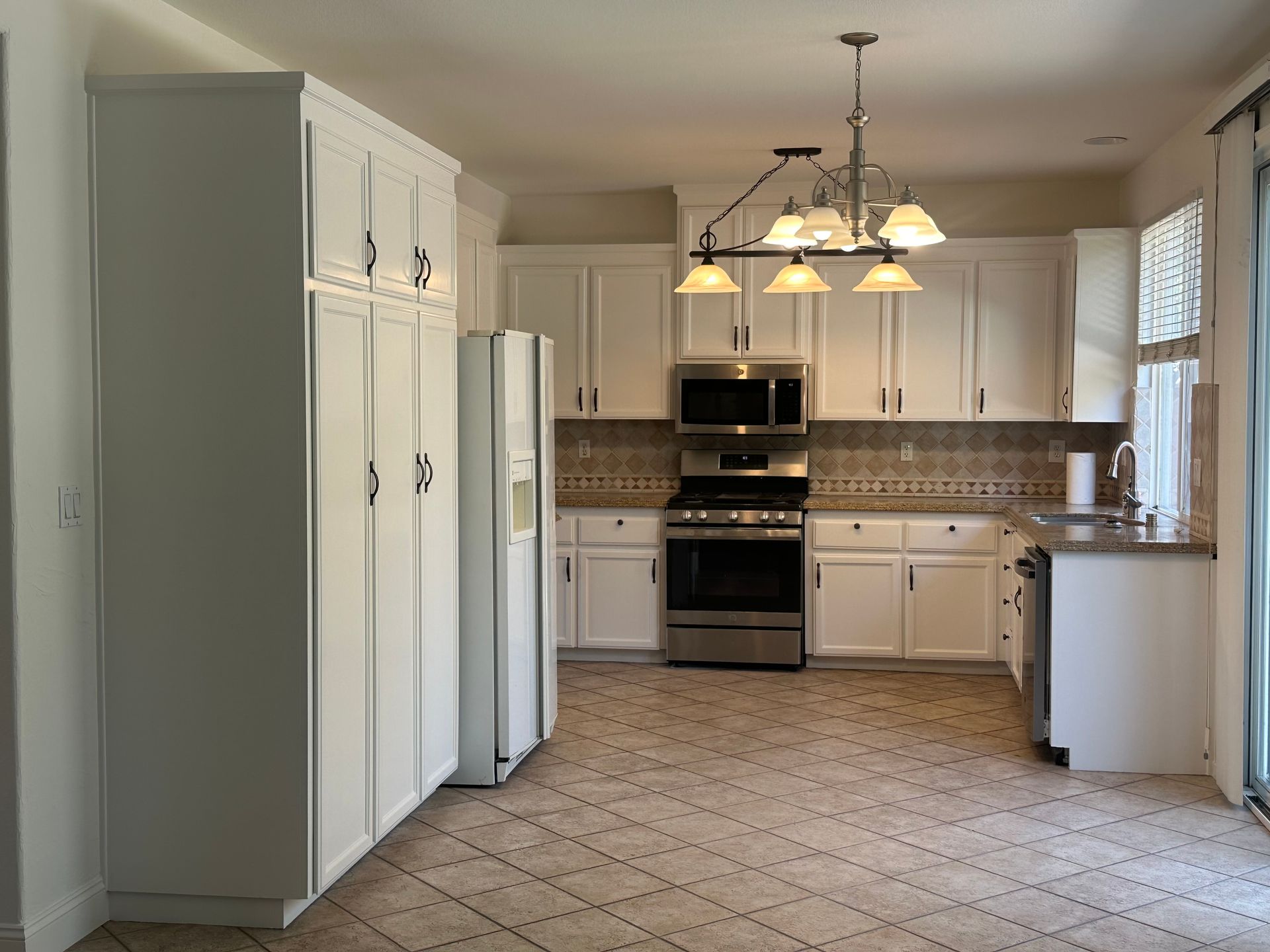 A kitchen with white cabinets , stainless steel appliances , a refrigerator , and a microwave.