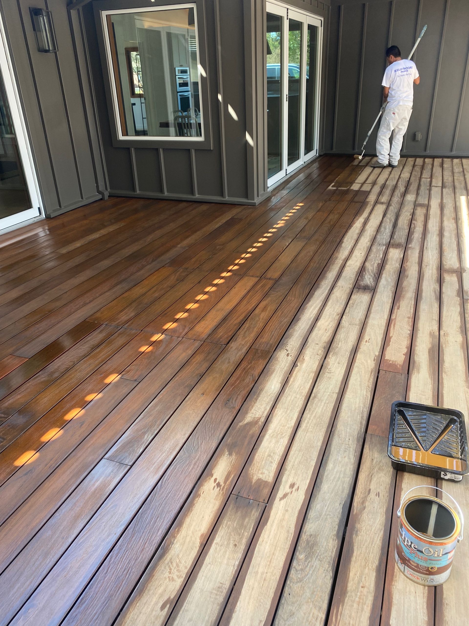 A man is painting a wooden deck with a broom.