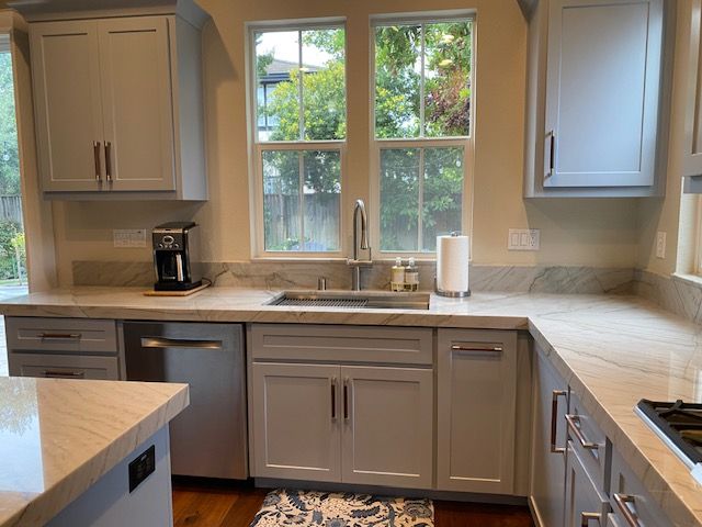 A kitchen with white cabinets , a sink , a dishwasher , and a window.