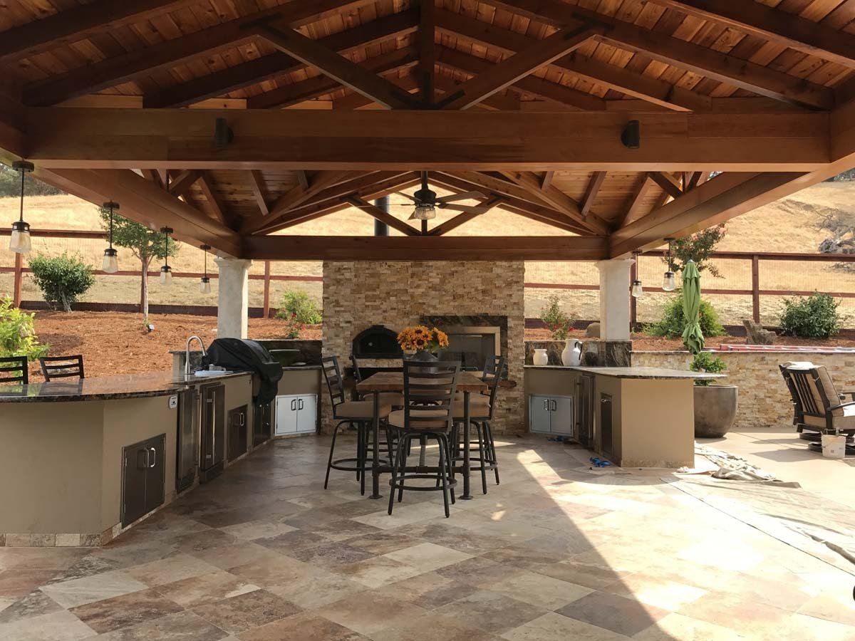 A large outdoor kitchen with a wooden roof and a pizza oven.