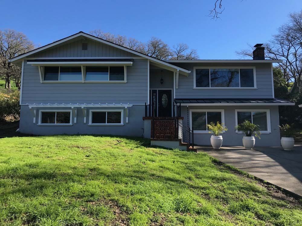 A house with a lot of windows is sitting on top of a lush green hillside.
