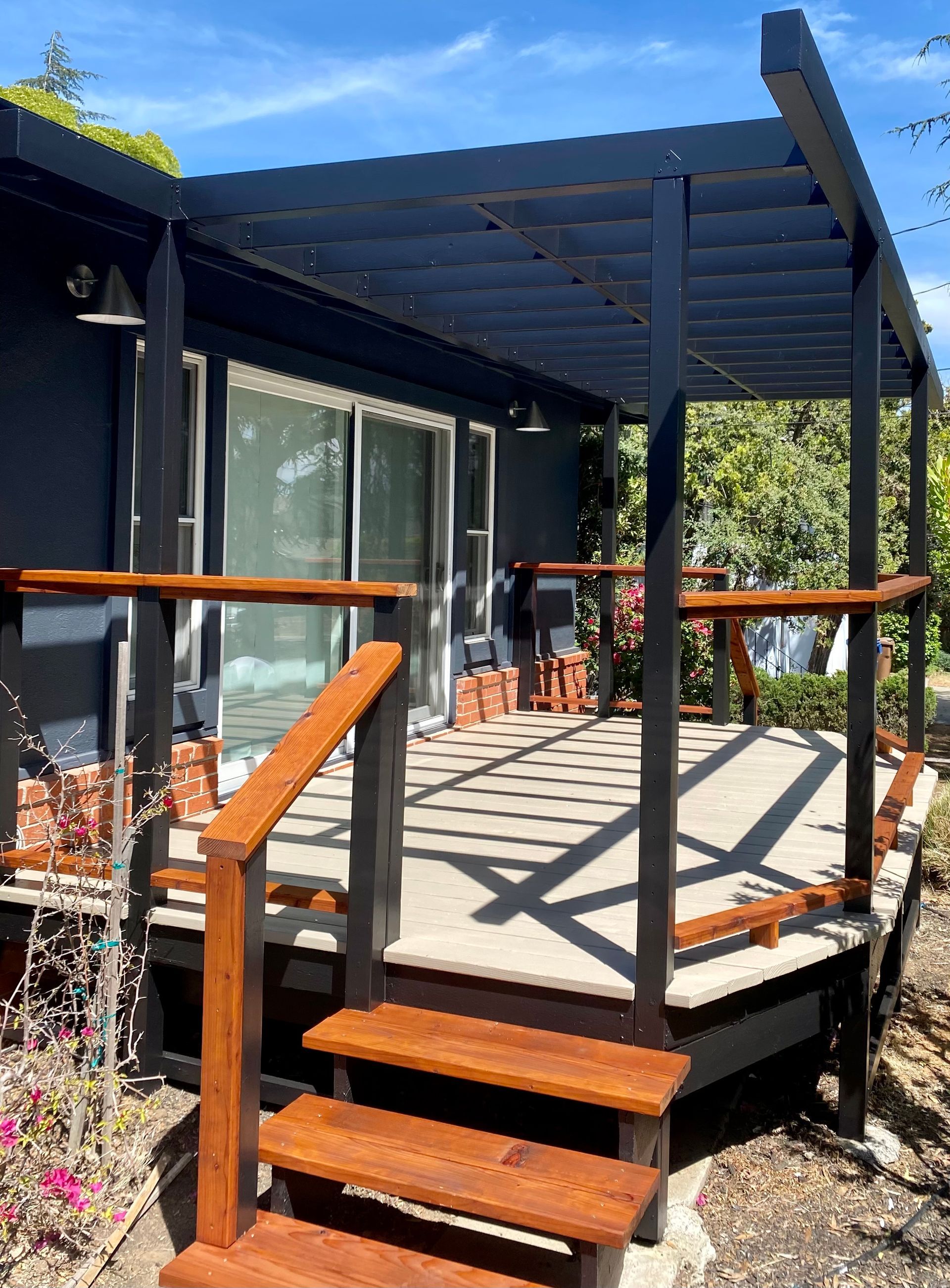 A black house with a wooden deck and stairs leading to it.