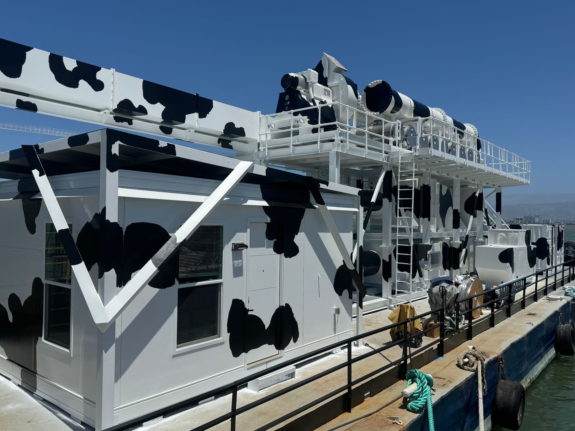 A white and black cow print boat is docked in the water.