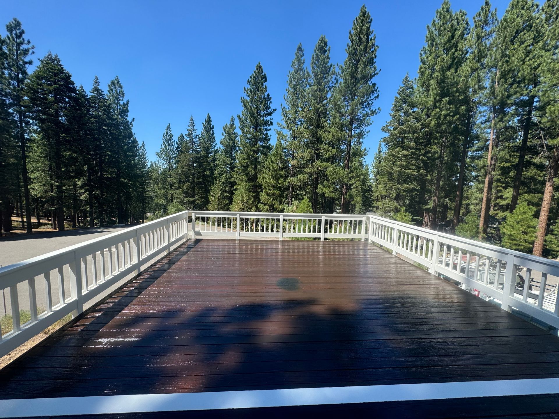 A wooden deck with a white railing and trees in the background