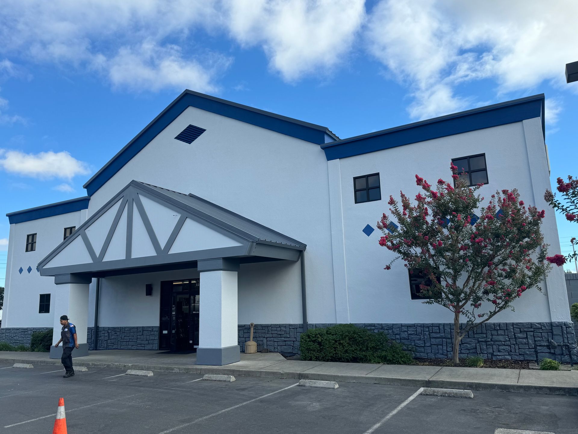A white building with a blue roof and a tree in front of it.