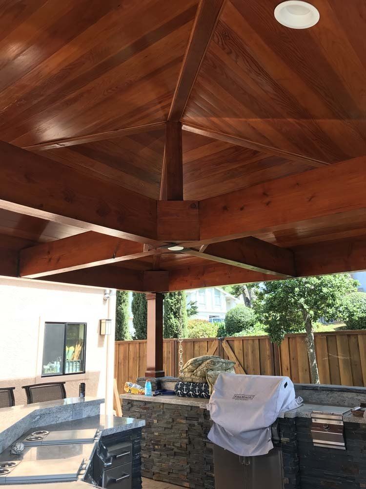 A wooden gazebo with a grill underneath it.