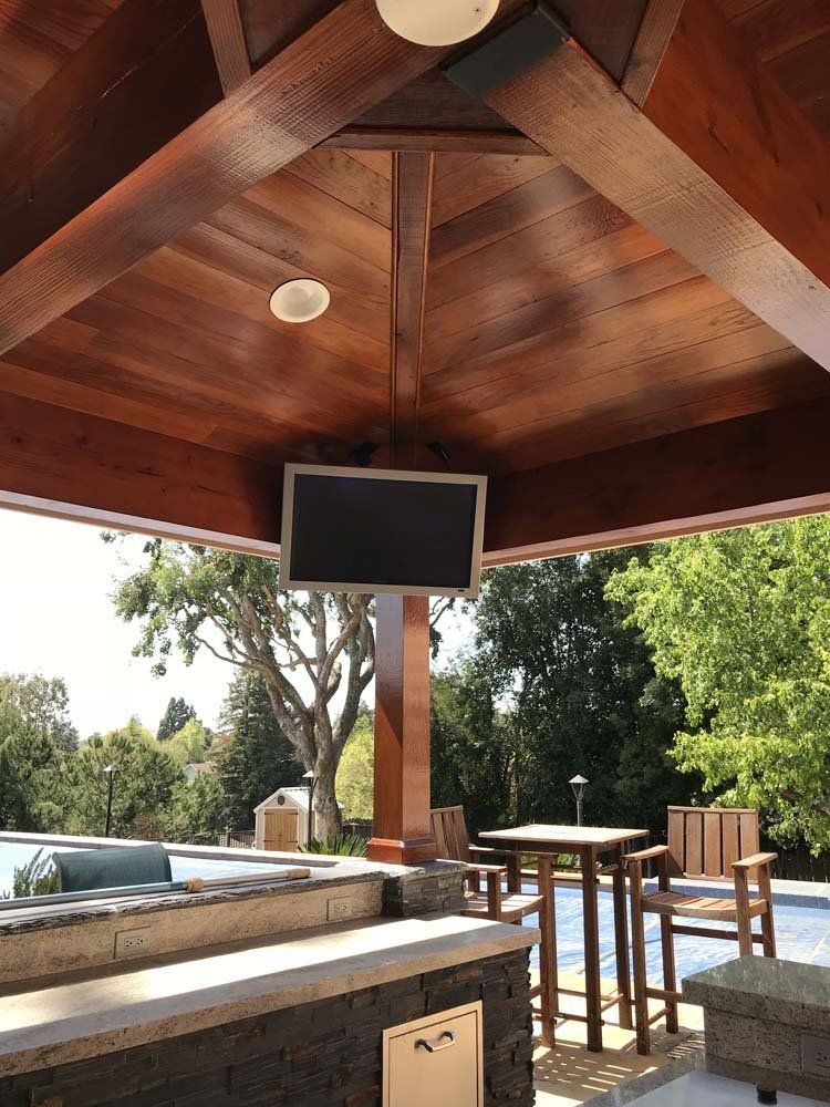 A large flat screen tv is hanging from the ceiling of a gazebo.
