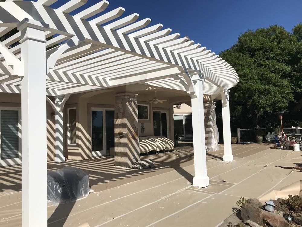 A white pergola is sitting on top of a patio next to a house.