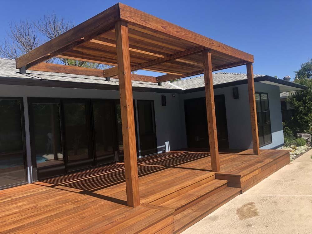 A wooden deck with a pergola over it is in front of a house.