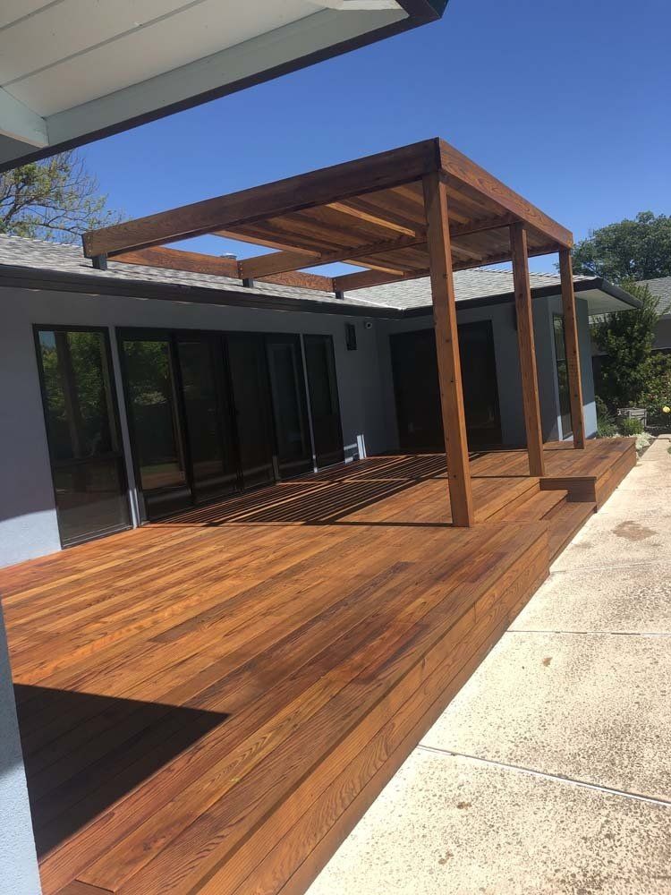 A wooden deck with a pergola on top of it in front of a house.