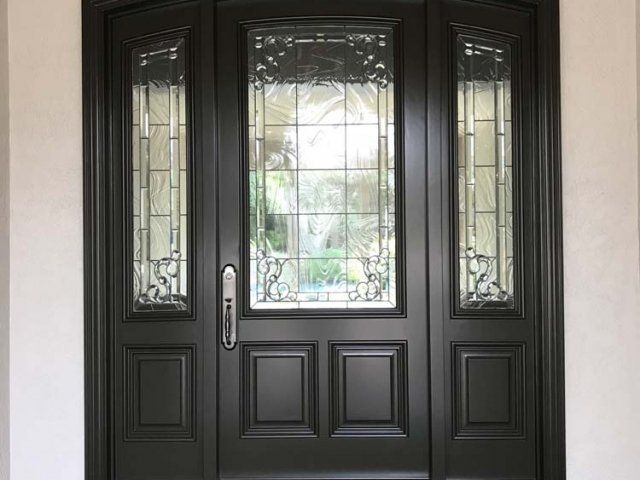 A black front door with stained glass windows is sitting on top of a white wall.