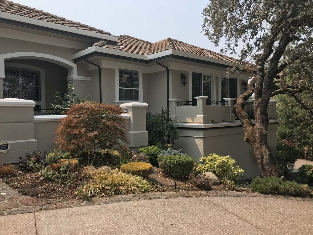 A large white house with a tile roof is surrounded by trees and bushes.