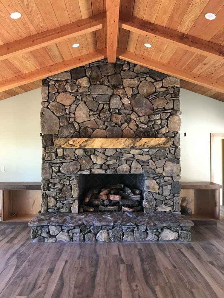 A large stone fireplace in a living room with a wooden ceiling.