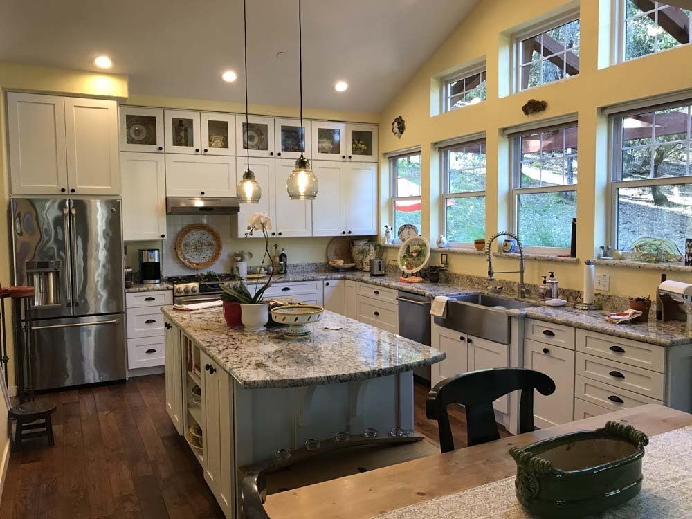 A kitchen with white cabinets , stainless steel appliances , granite counter tops and a large island.