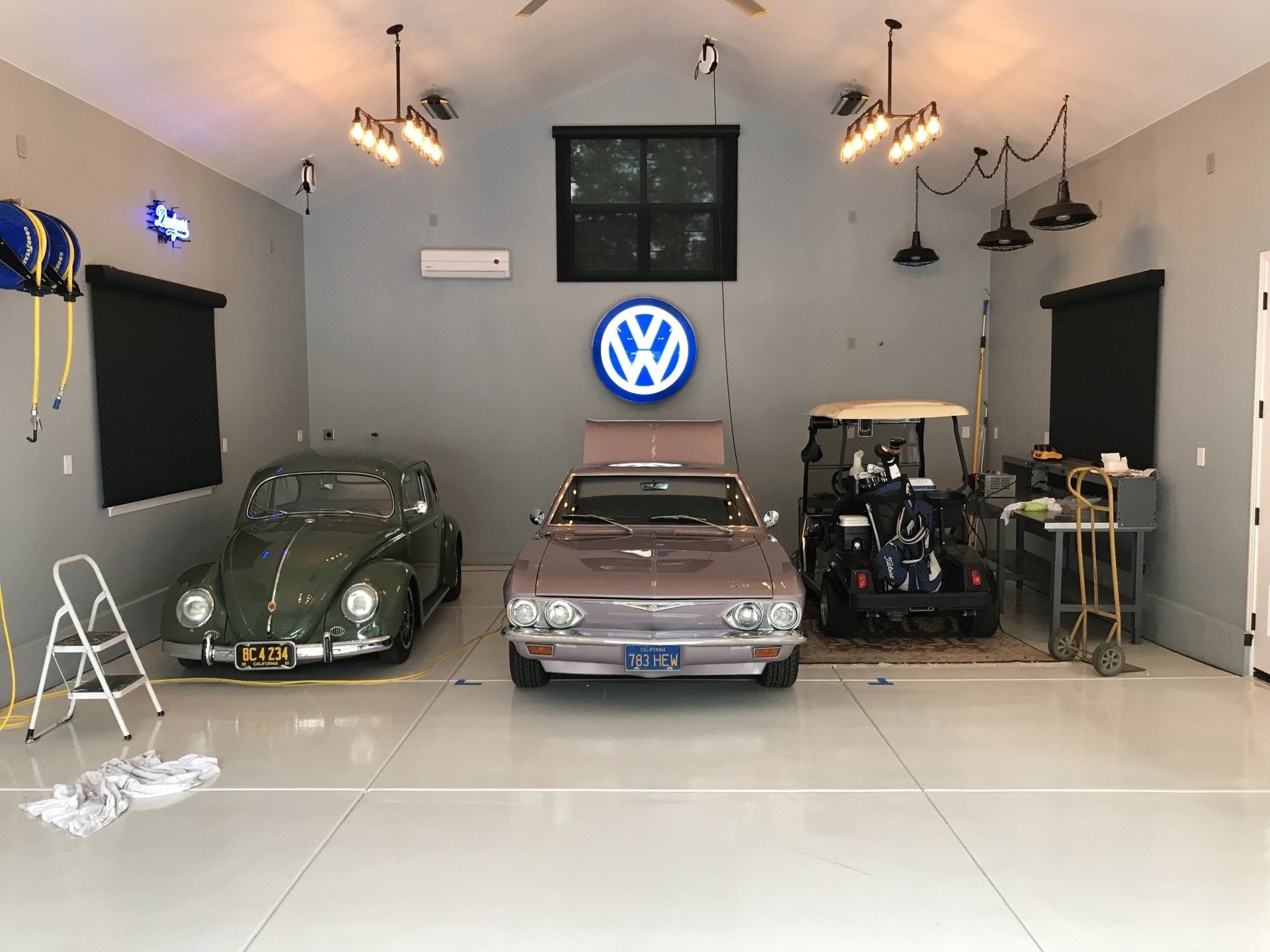 Two cars are parked in a garage with a vw logo on the wall.