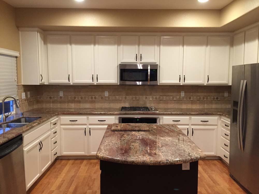 A kitchen with white cabinets , granite counter tops , stainless steel appliances and a large island.