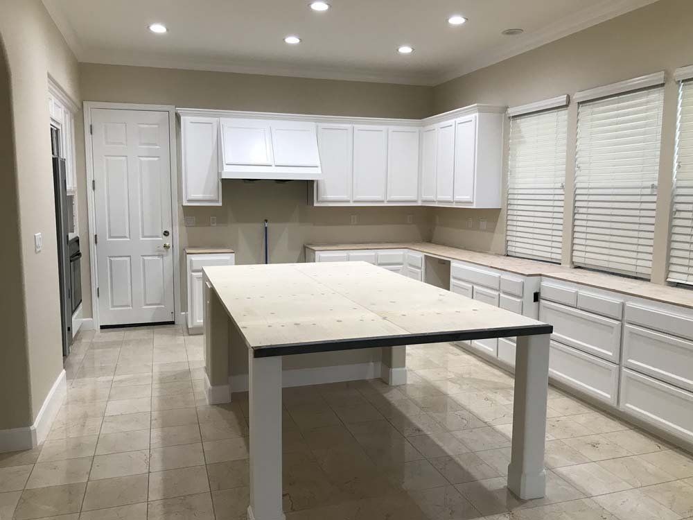 A kitchen with white cabinets and a large table in the middle.