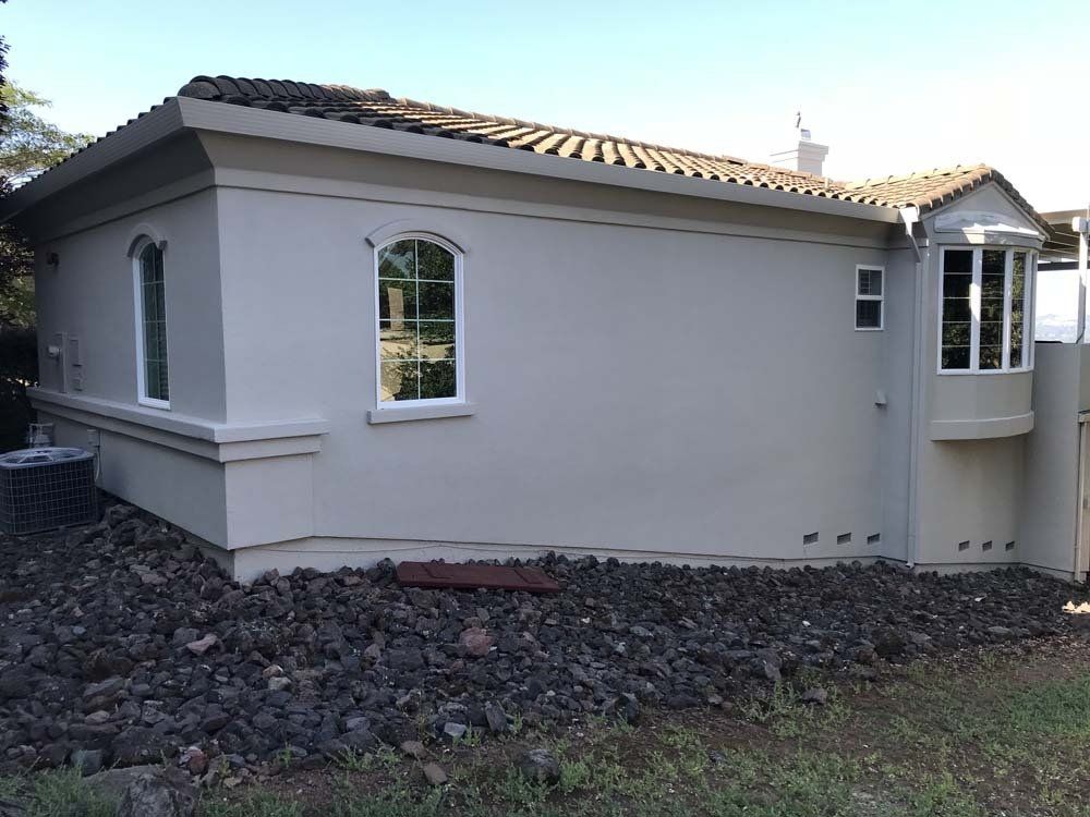 A small white house with a lot of windows is sitting on top of a pile of rocks.