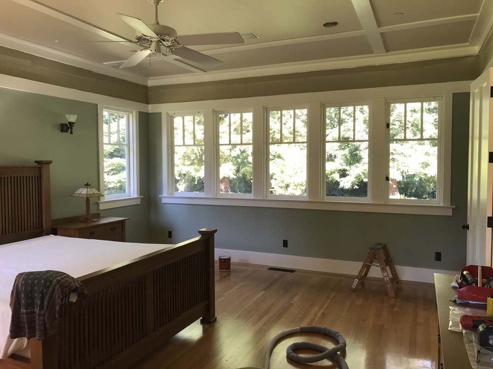 A bedroom with a bed , ceiling fan , and lots of windows.