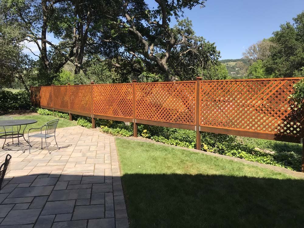 A wooden fence surrounds a patio with a table and chairs.