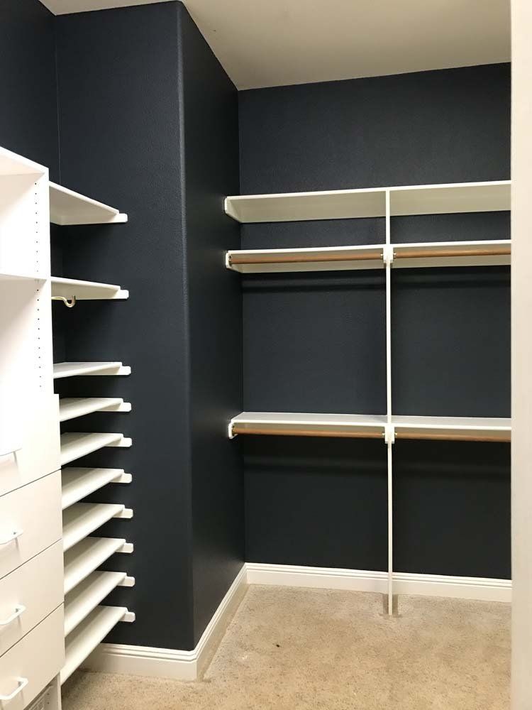 A walk in closet with blue walls and white shelves