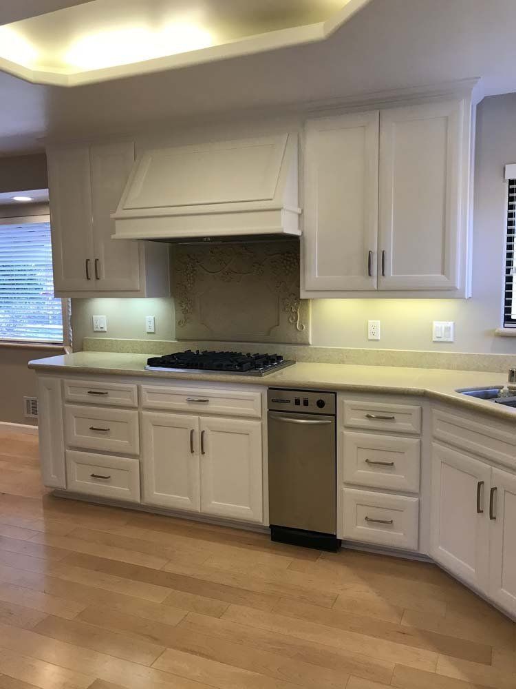 A kitchen with white cabinets , a stove , a dishwasher , and a window.