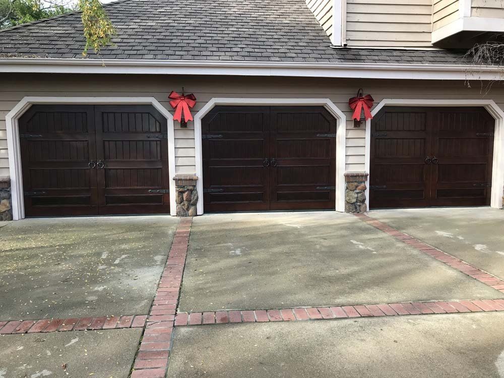 Three garage doors with red bows on them are sitting next to each other on the side of a house.