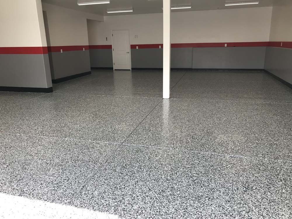 A large empty garage with a gray and red floor.