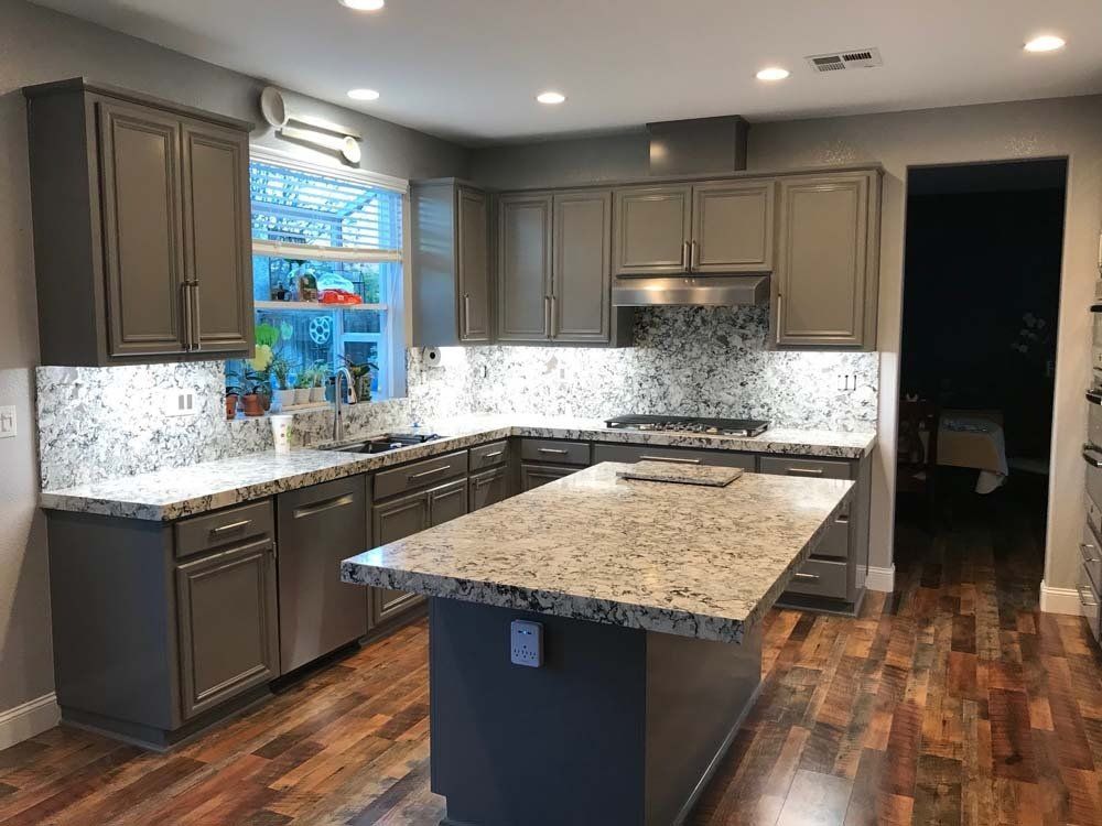 A kitchen with gray cabinets , granite counter tops , stainless steel appliances and a large island.