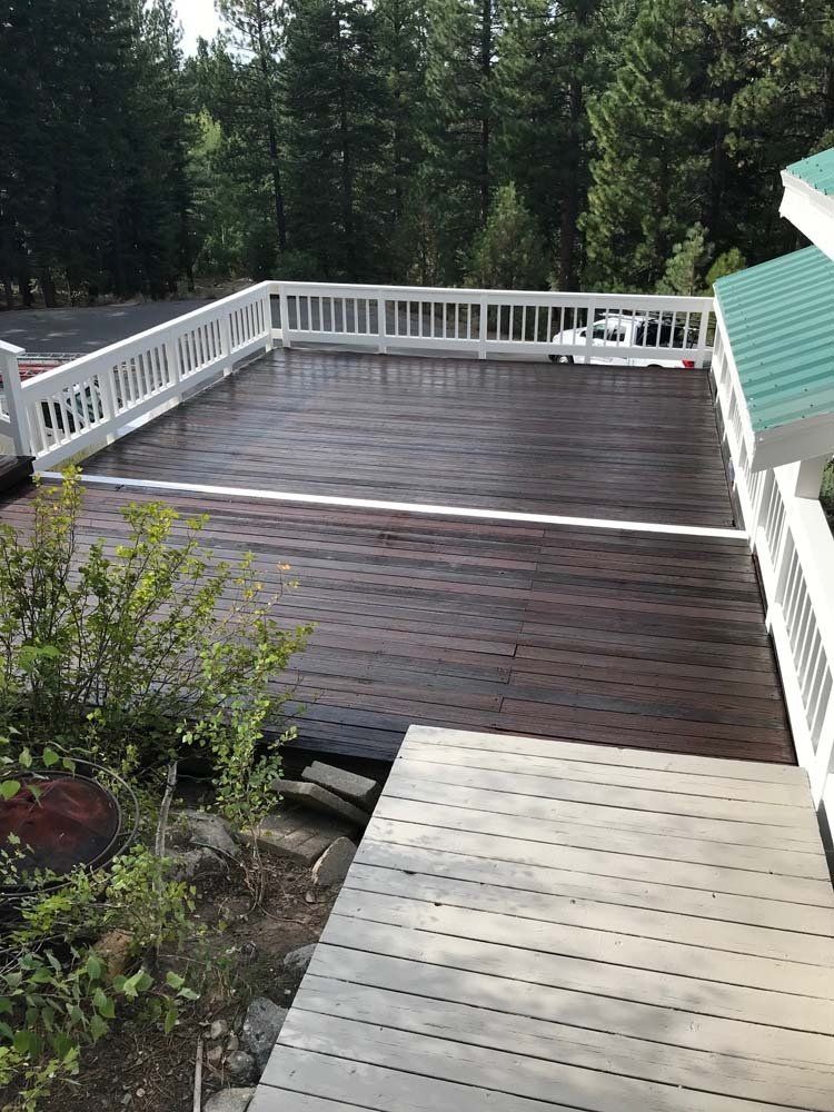 A large wooden deck with a white railing and trees in the background.