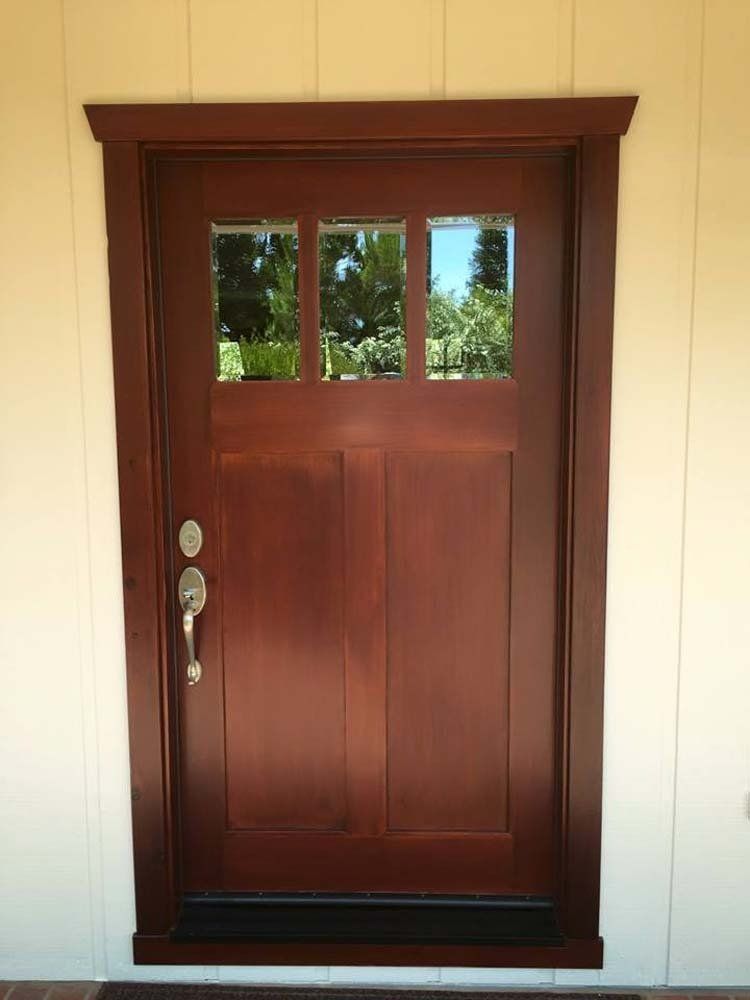 A wooden door with three windows on a white wall